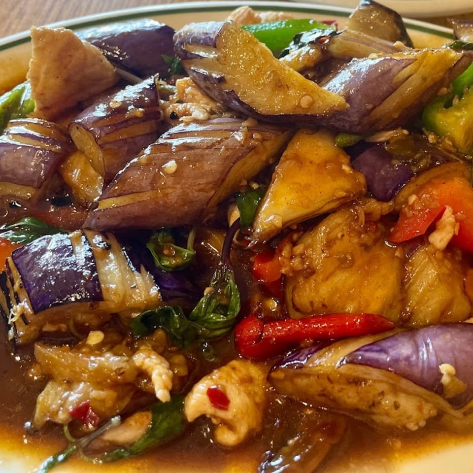 Close-up of Thai eggplant stir-fry with chicken, bell peppers, and basil in a savory sauce.