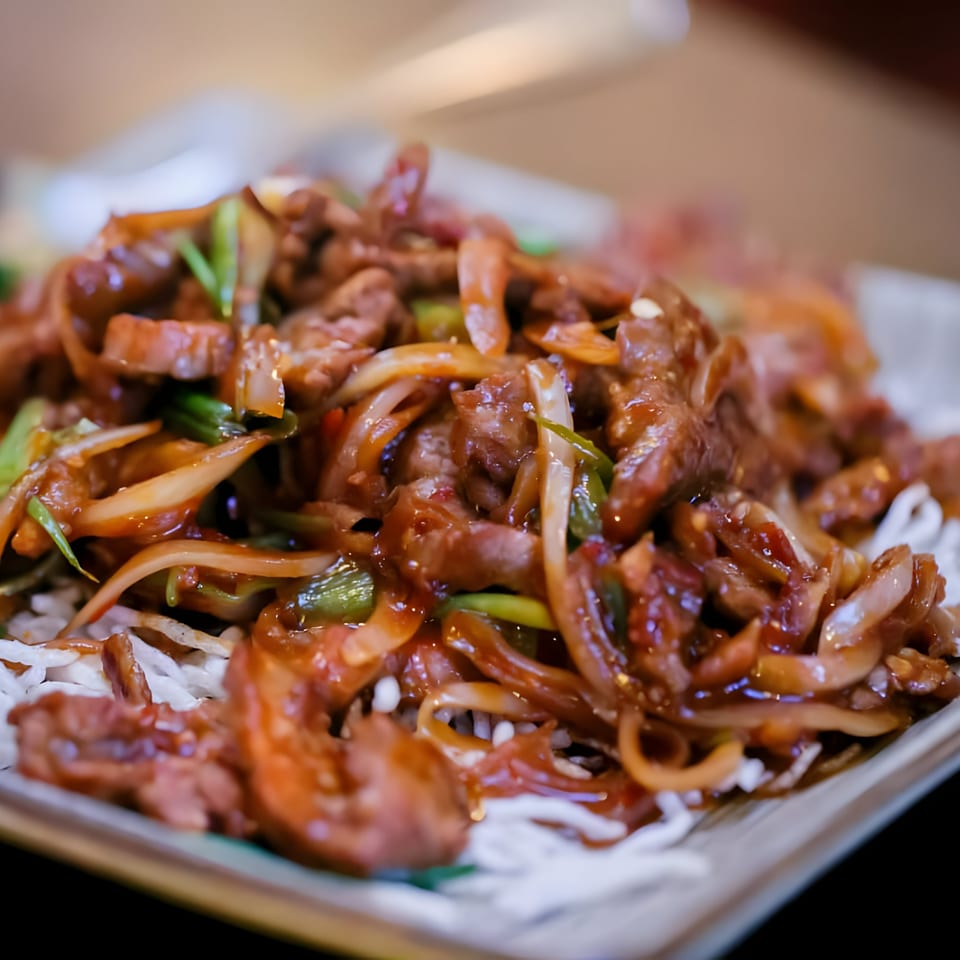 Close-up of a Thai beef dish with onions and green scallions, served over white noodles.