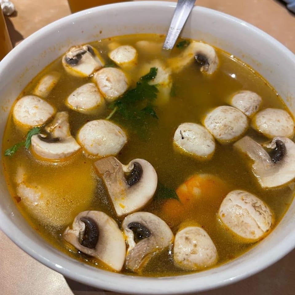 A white bowl of West Covina Thai Cuisine's Tom Yum soup with mushrooms and meatballs.