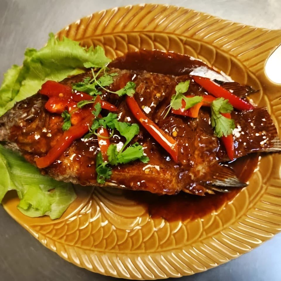 Whole fried fish with sweet chili sauce, red peppers, and cilantro on a leaf-shaped plate.