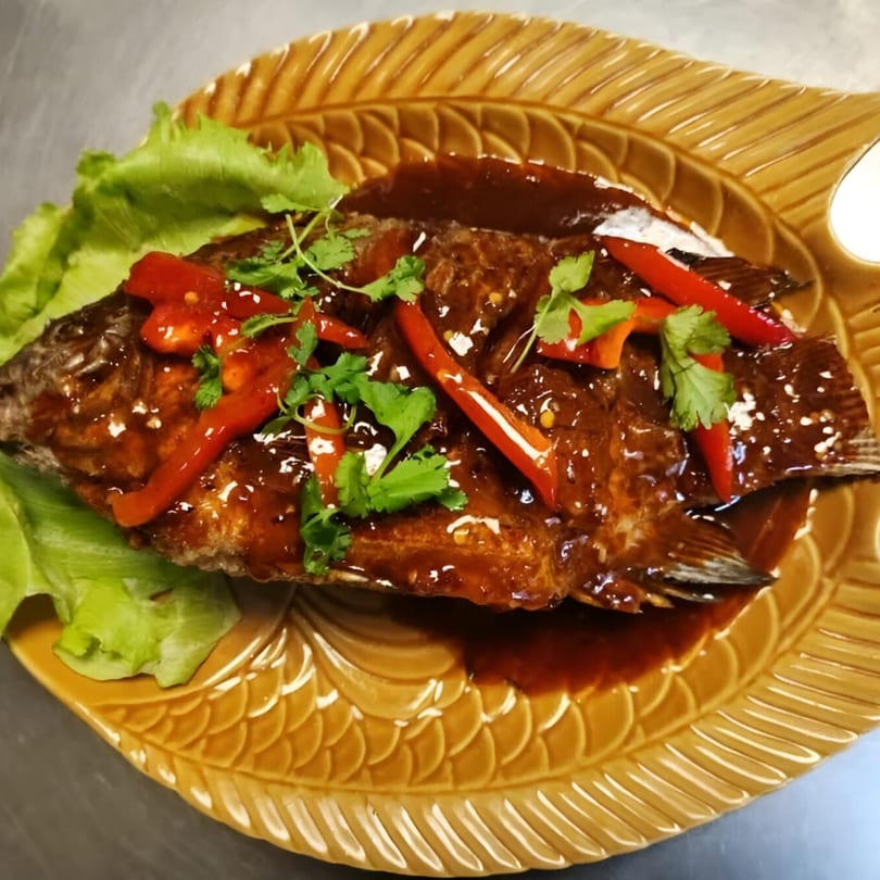 Whole fried fish with sweet chili sauce, red peppers, and cilantro on a leaf-shaped plate.