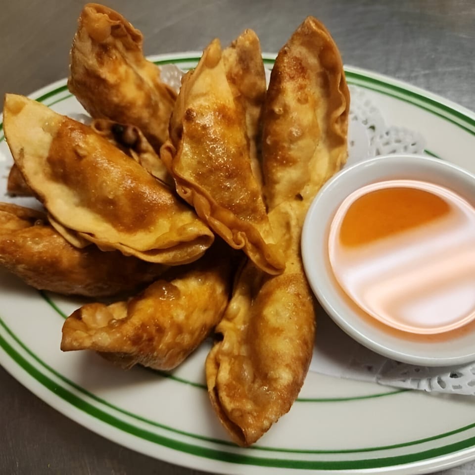 Golden-fried Thai dumplings with a side of sweet chili dipping sauce on a white plate.