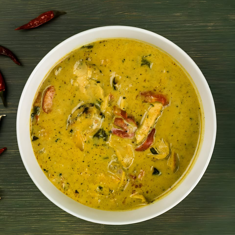 Overhead view of a bowl of yellow Thai curry with chicken and red peppers, garnished with dried chilies.