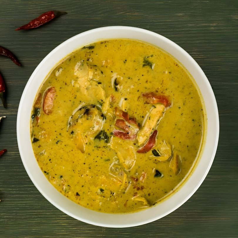 Overhead view of a bowl of yellow Thai curry with chicken and red peppers, garnished with dried chilies.